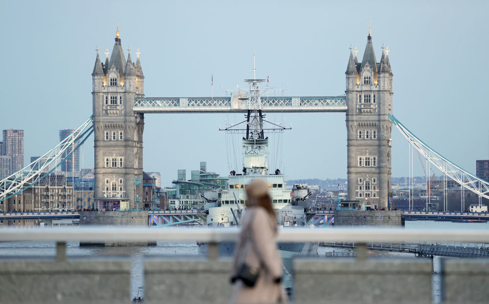 一名女子在英国伦敦横跨泰晤士河的伦敦桥上行走，不远处是地标建筑——塔桥。
