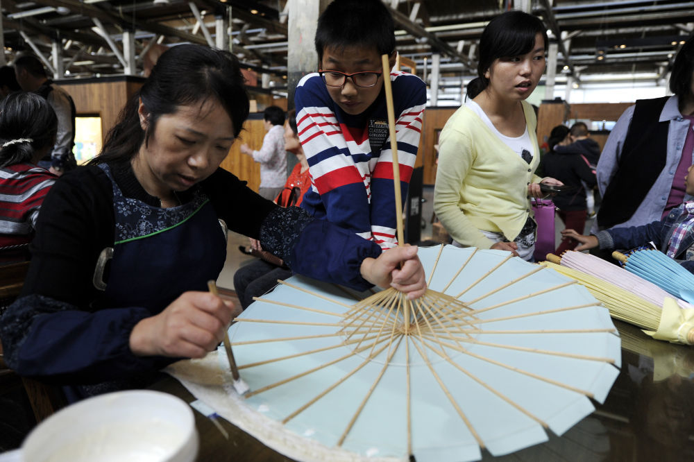 2014年10月18日，游客和市民在浙江杭州举办的2014中国大运河庙会上参观西湖绸伞制作技艺展示。
