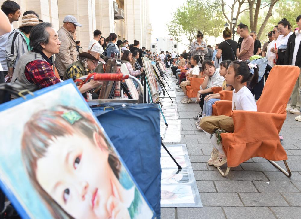 5月1日，游客在哈尔滨中央大街上画肖像画。新华社发 （刘洋摄）