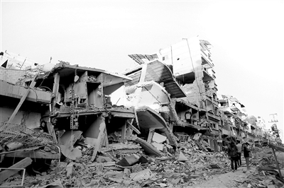 3月6日,在加沙地带南部城市汗尤尼斯,人们经过建筑废墟