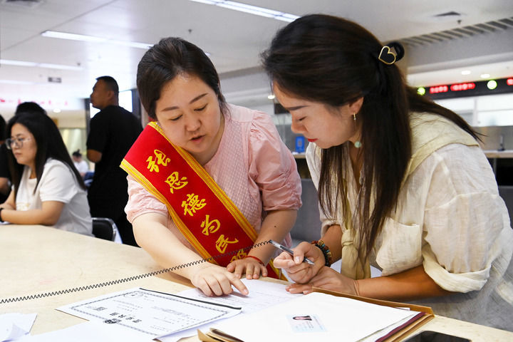 延安市宝塔区行政审批服务局张思德为民服务队工作人员杨姣（左）在延安市政务服务中心帮助群众办理业务（2024年8月9日摄）。新华社记者 邹竞一 摄