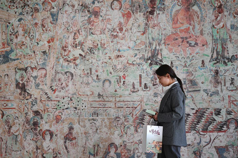 敦煌研究院文物数字化保护团队工作人员从一幅高保真复制壁画前走过。