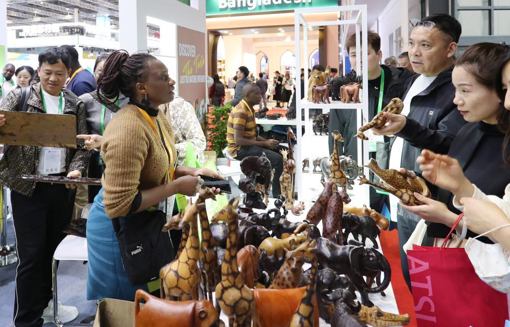 2023年11月6日，来自津巴布韦的艾薇顿丝·察卡瓦在展台向参观者介绍木雕展品。这是她第一次来到中国上海参加进博会，这些木雕都是她的哥哥在家里制作的，她想通过进博会为哥哥的木雕作品找到好的销路。新华社记者方喆摄