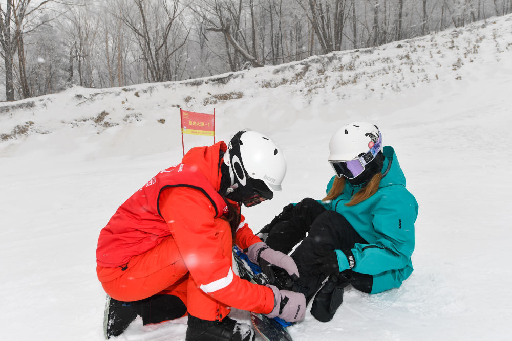 ↑2023年11月23日，滑雪教练王雪（左）在北大湖滑雪度假区帮学员调整雪具。新华社记者 张楠 摄