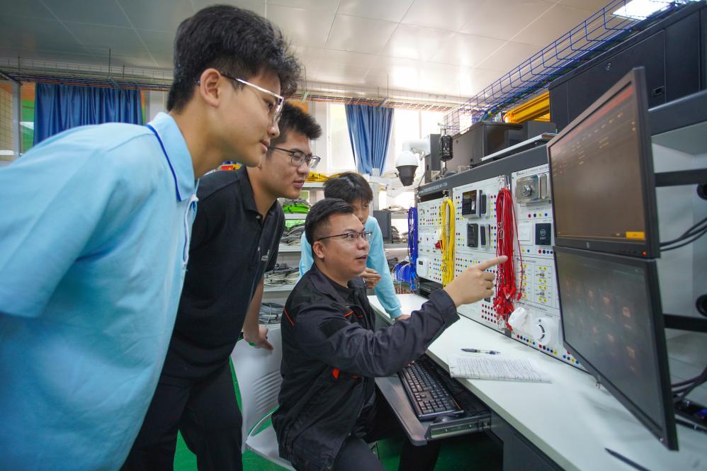 梁嘉伟（前排右一坐者）正在向学生传授技术课程。新华社记者胡拿云 摄