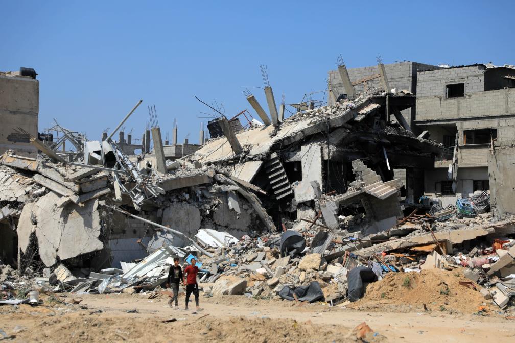 4月16日，在加沙地带南部城市汗尤尼斯，人们走过损毁的建筑。新华社发（里泽克·阿卜杜勒贾瓦德摄）