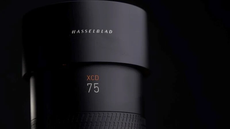 Close-up of a black Hasselblad camera lens with the brand name engraved on the upper cylinder. The text 