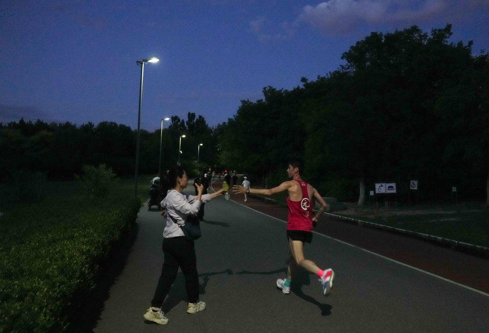 6月24日，在北京奥林匹克森林公园，栾玉帅（右）在跑步训练中从妻子手中接过运动饮料。