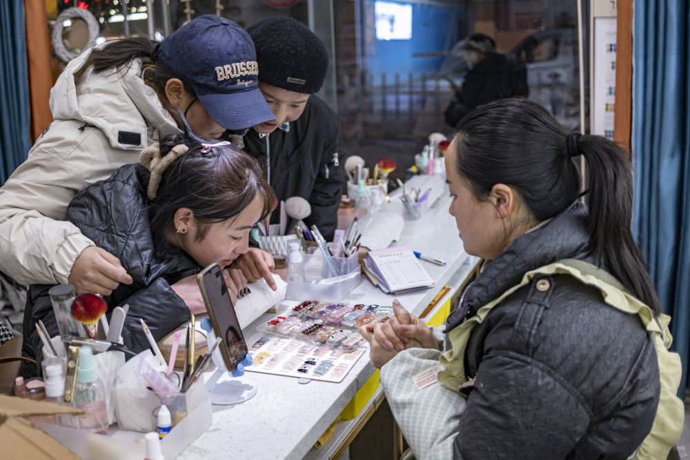 在拉萨市中心的一家美甲店，丹增（左下）正在挑选指甲款式（2024年1月27日摄）。新华社记者 孙非 摄