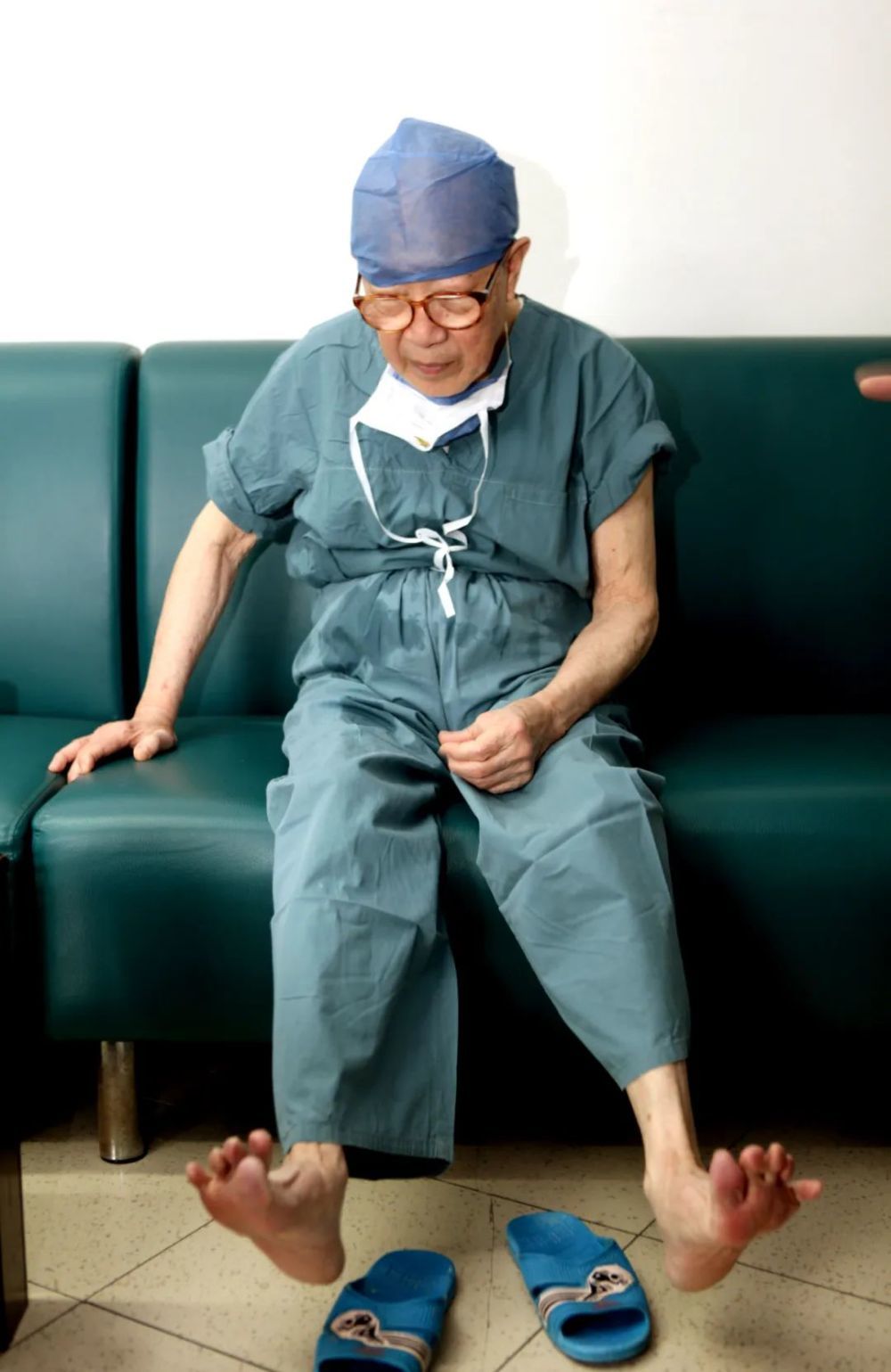 吴孟超走下手术台，坐在医生休息室的沙发上活动站累了的双脚。新华社发（张鹏 摄）
