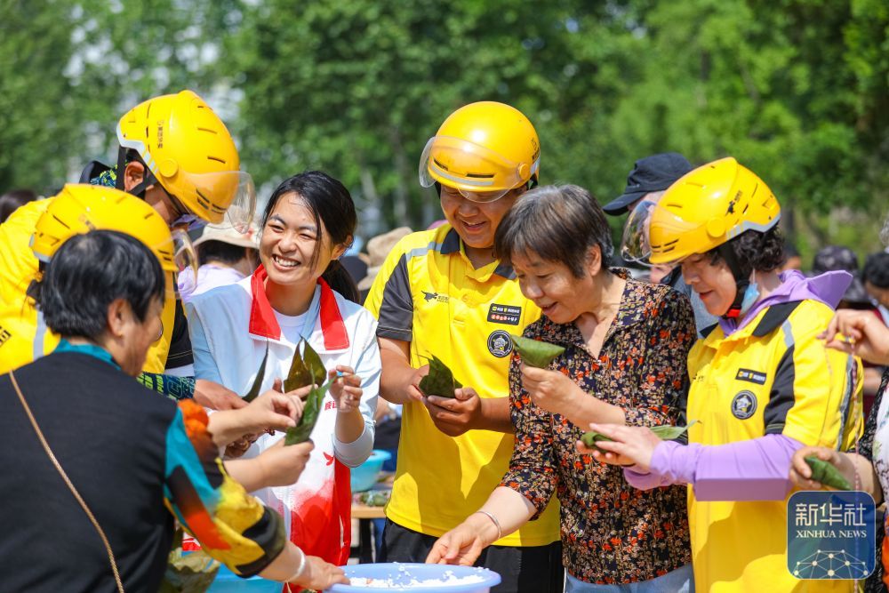 ↑ 5月24日，在山东省青岛市城阳区城阳街道顺德居社区举办的迎端午主题活动中，外卖骑手和社区居民一起包粽子。新华社发（张鹰摄）