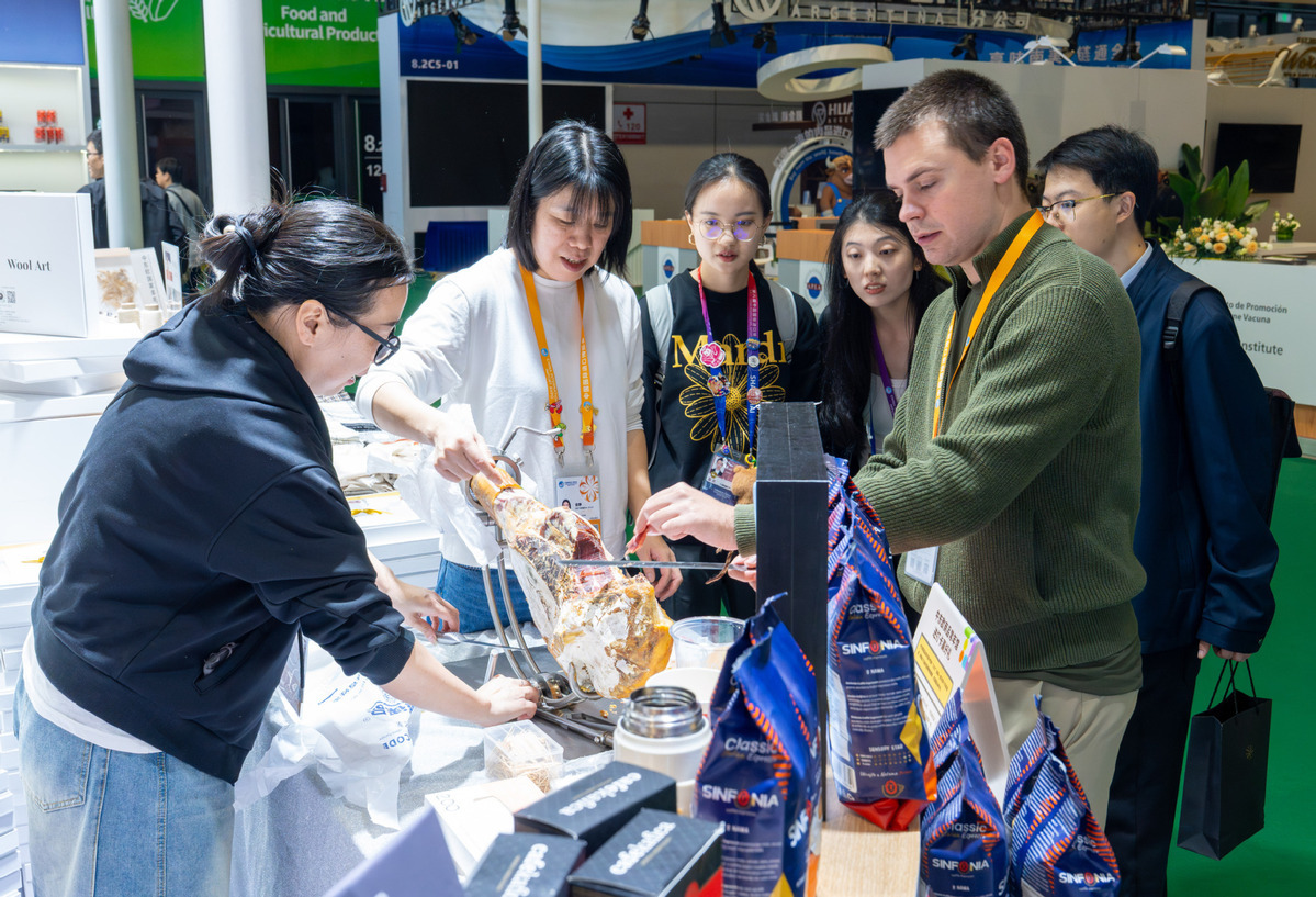 2025年11月5日,在第八届进博会农食产品展区,参展商为观众介绍伊比利亚火腿。(图片来源:新华社)