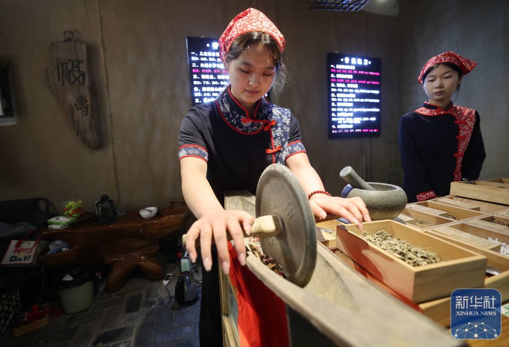 ↑ 5月24日，在山东省临沂市沂南县铜井镇竹泉村，传统手工艺人在捣碎中药材，准备制作香囊。新华社发（王彦冰摄）