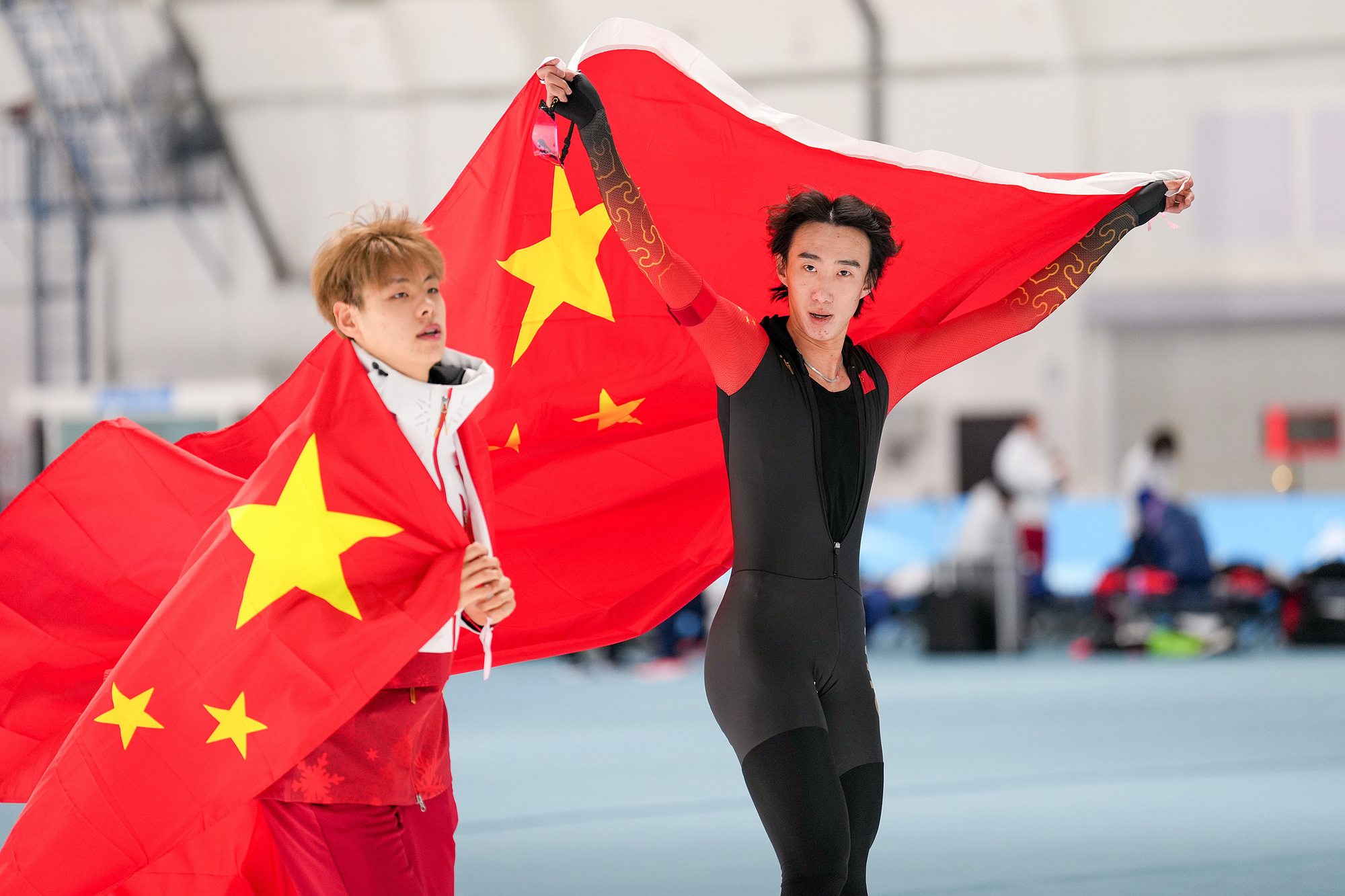 在亚冬会速度滑冰男子5000米决赛中获得金牌的吴宇和获得银牌的刘瀚彬身披国旗绕场