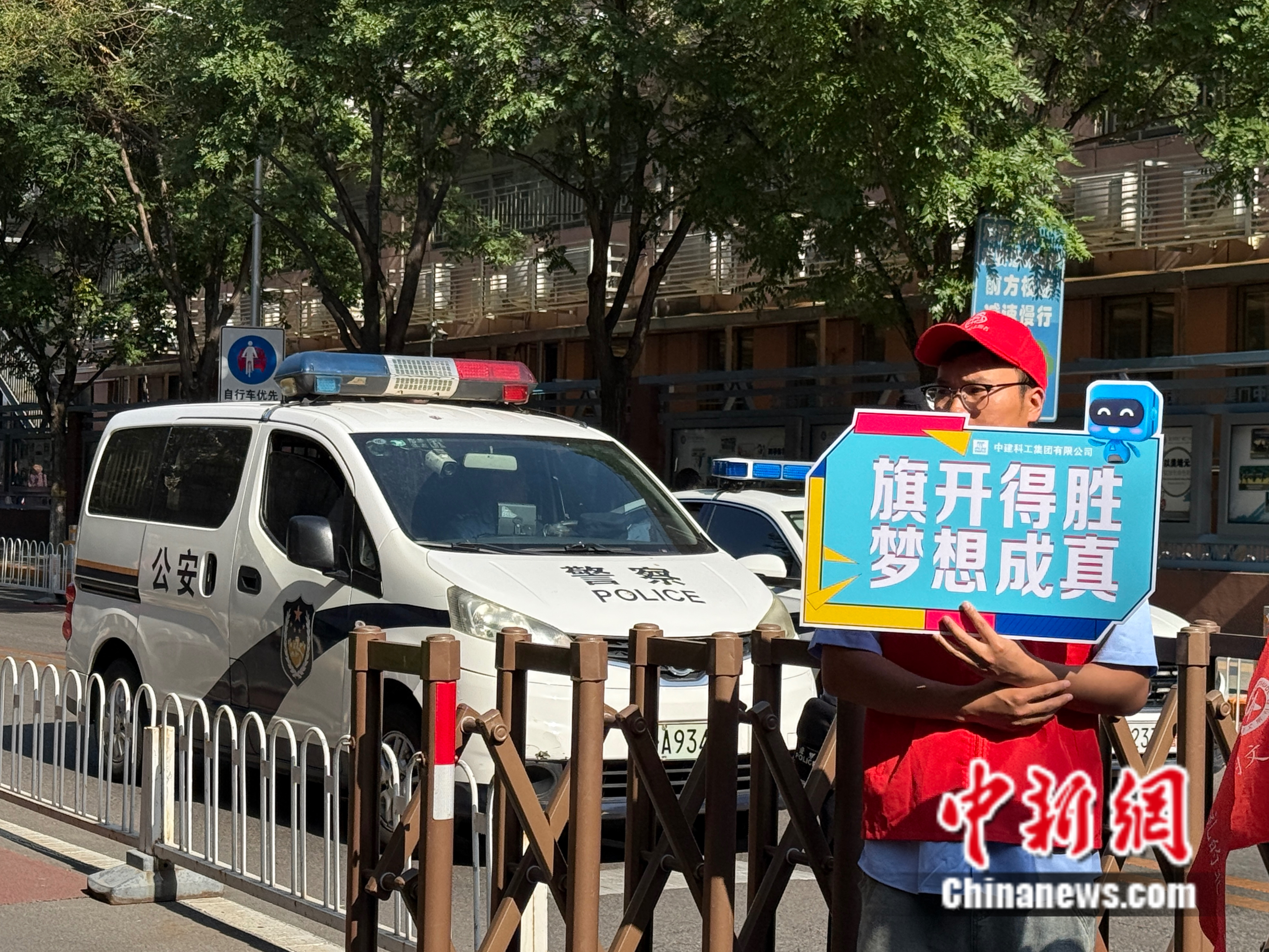 6月7日,北京市广渠门中学,志愿者举着印有“旗开得胜 梦想成真”的牌子,祝福考生。邵萌 摄