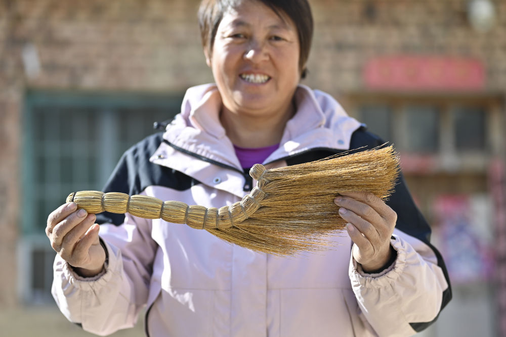 ↑村民程娇梅展示秦海松为她制作的扫帚（2025年12月1日摄）。