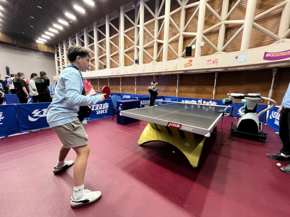 4月12日,美国青少年在上海国际乒联博物馆和中国乒乓球博物馆的乒乓球发球机器人前体验接球。新华社记者有之炘摄