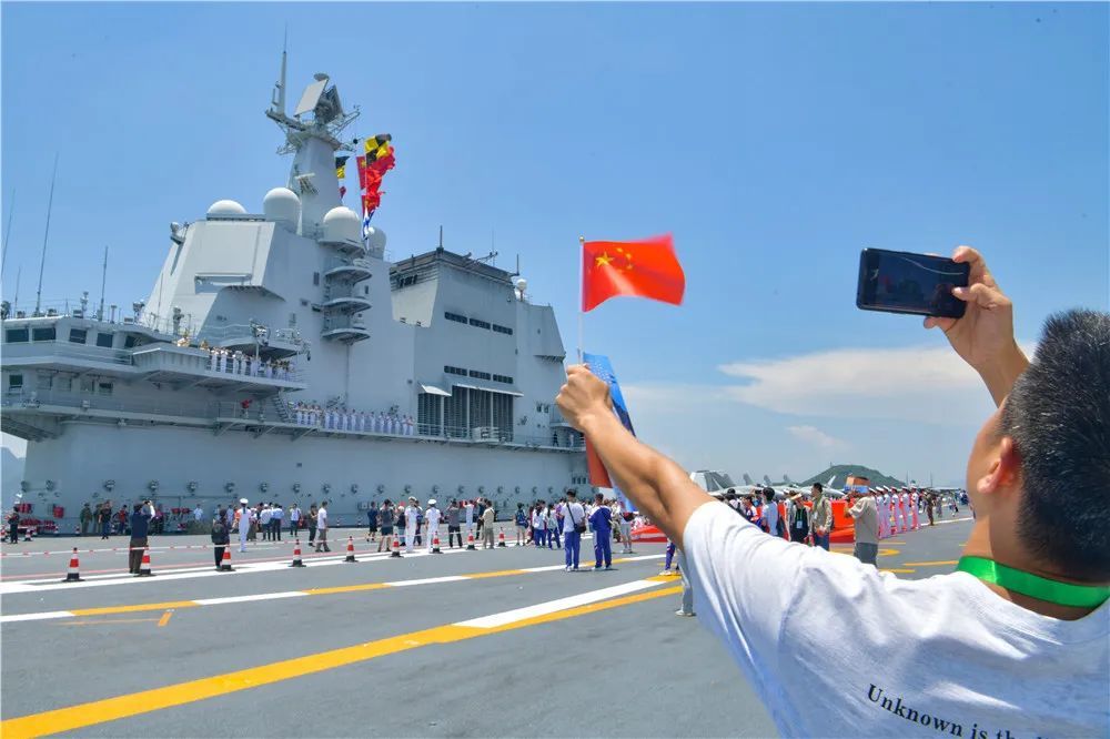 ▲山东舰甲板上舰员演唱《我和我的祖国》,香港市民挥舞国旗打卡留影,交相呼应 杨科 摄