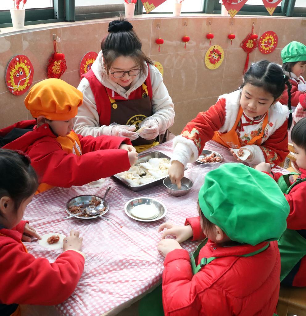 2月27日，江苏省宜兴市均陶幼儿园的老师带领孩子们包“龙耳”。新华社发（丁焕新摄）