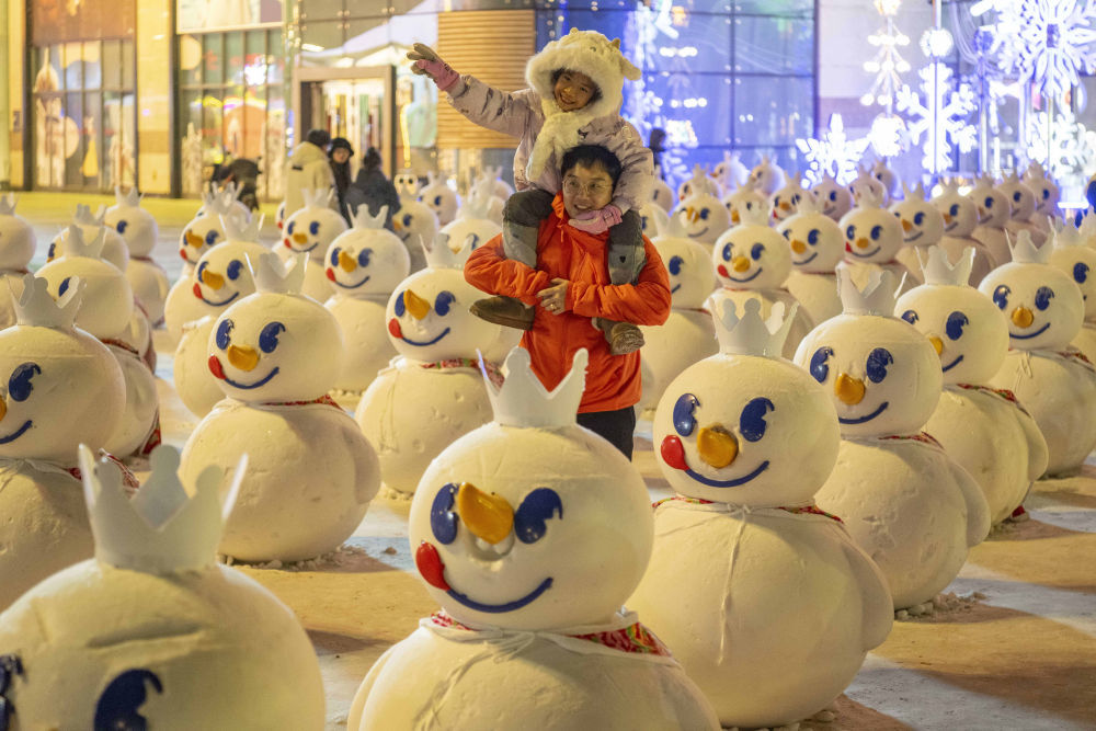 ↑1月3日，在哈尔滨市道里区群力大道，游客在一家商场前的“雪人军团”处游玩。新华社记者 谢剑飞 摄