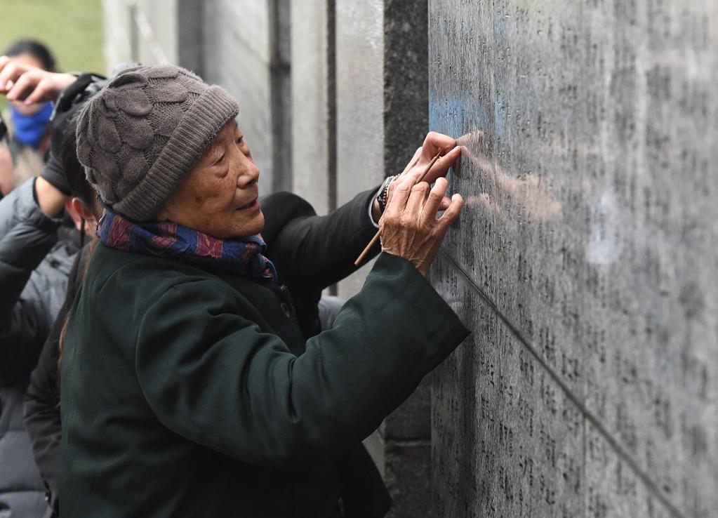 ↑2018年12月10日，在侵华日军南京大屠杀遇难同胞纪念馆举行的死难者遗属家祭活动中，夏淑琴给遇难者名单墙上亲人的名字添漆。新华社记者 孙参 摄