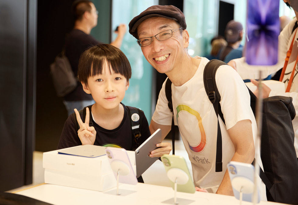 Apple 银座零售店内，一个孩子和一名成年人拿着 iPad，站在 iPhone 17 展示桌旁。