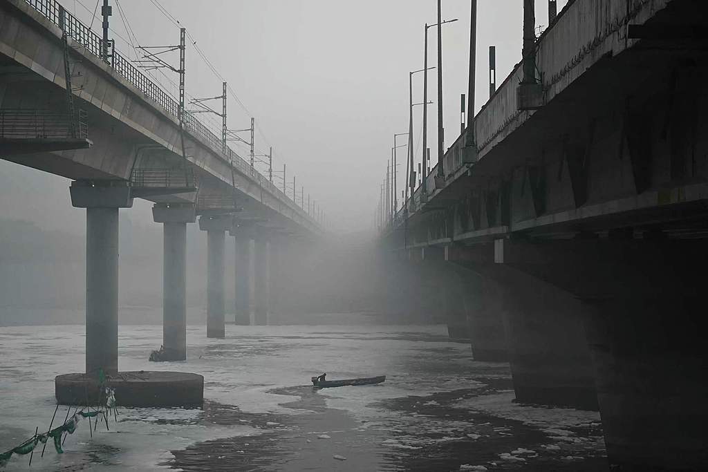 当地时间2025年11月20日,印度新德里,一个雾蒙蒙的早晨,一名市政工作人员划船穿过亚穆纳河被污染泡沫覆盖的水域。视觉中国 图