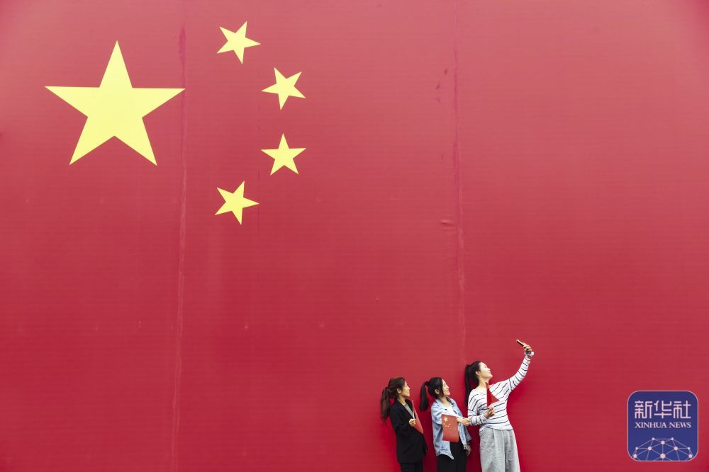 ↑ 10月1日,在河南省济源市那些年小镇,游客与国旗合影。新华社发(苗秋闹摄)