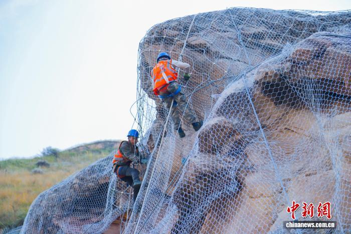 图为兰州铁路局兰州西工务段的工作人员攀爬在近百米高、看似直立的石质山体上,为山体加装柔性主被动防护钢丝网。王光辉 摄