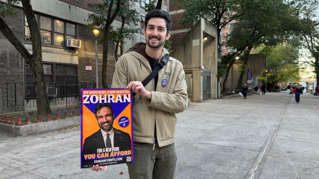 11月4日,支持者在美国纽约一个投票站外展示候选人祖赫兰·马姆达尼的竞选海报(手机拍摄)。新华社 图