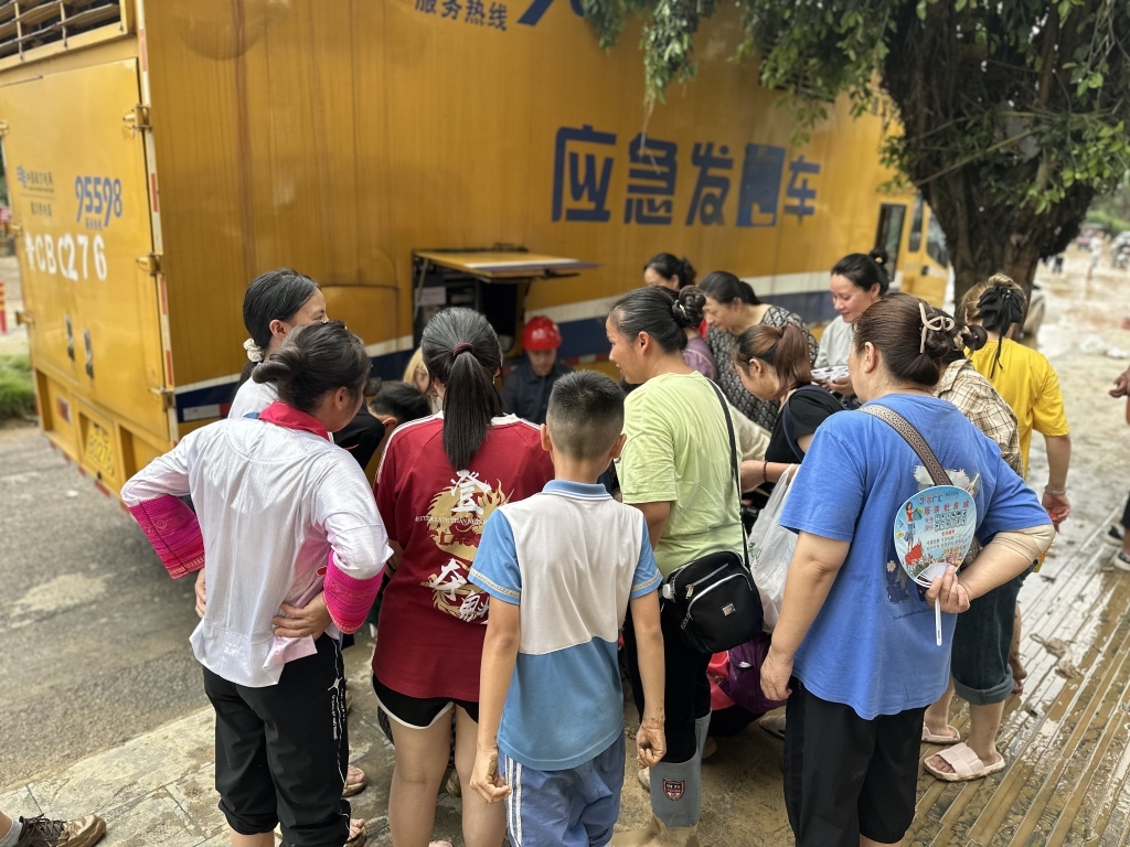 6月24日下午起,榕江县全城停电断网。25日上午,居民们在应急发电车旁为手机充电。