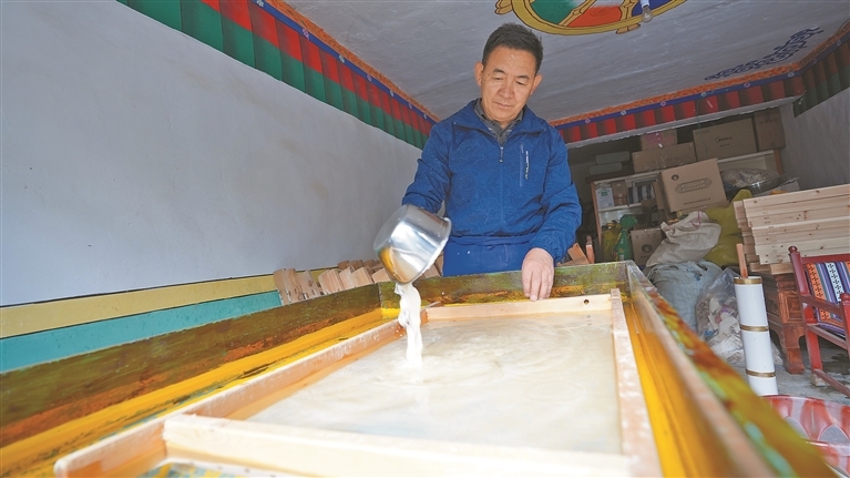 图为阿旺曲央将纸浆倾倒在帘上。