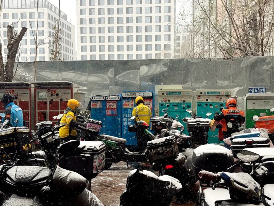 12月12日,下雪的北京,丰台区丰科万达商圈附近电动车停车场、换电站出现拥堵,骑手忙碌地取、送订单,或者边休整边等待订单。 摄影/本刊记者 王诗涵