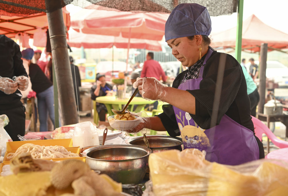 4月13日，一位商贩在新疆于田县先拜巴扎镇农牧民运动场为顾客制作面食。新华社记者 胡虎虎 摄