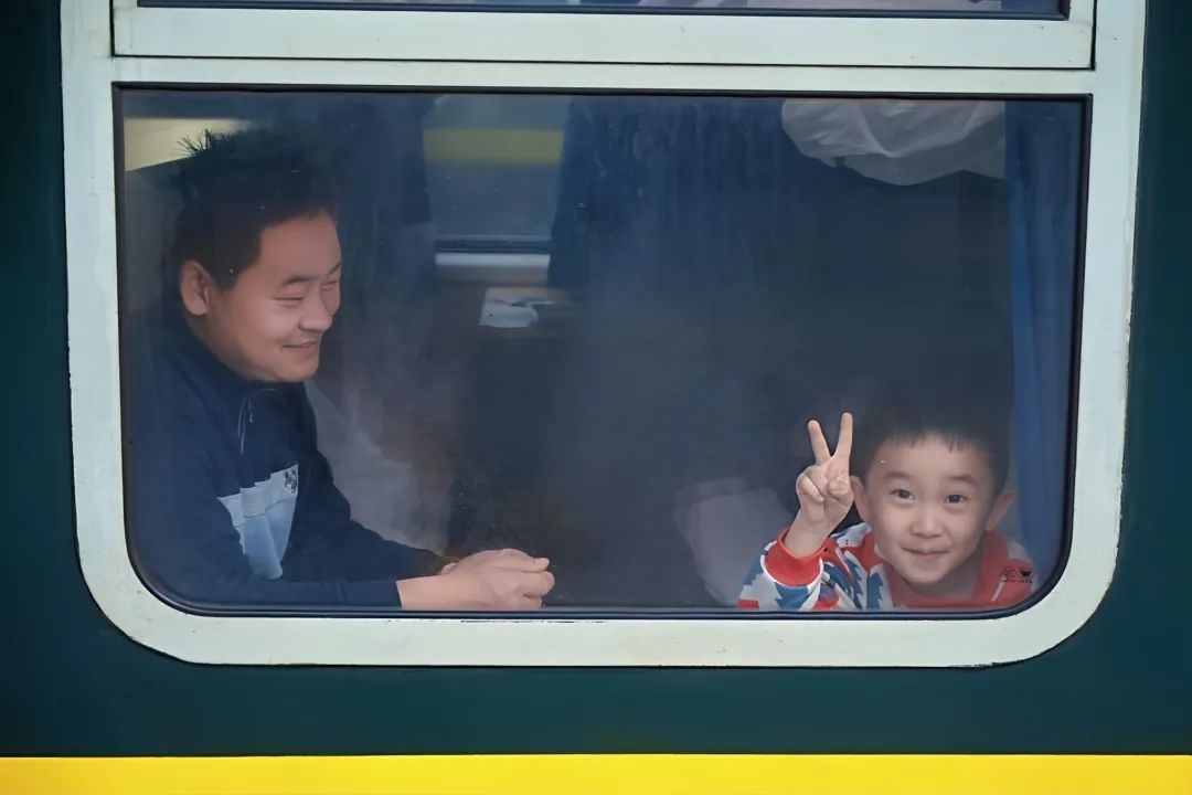 在火车缓缓启程前的瞬间,镜头捕捉到了这无比温馨的一幕。车厢内,父亲眉眼弯弯,笑意藏着无尽的温柔。可爱的孩子俏皮地比出“V”字手势,清澈明亮的眼眸满是对旅程的期待。这一方小小的车窗,框住了此刻的温暖与美好。