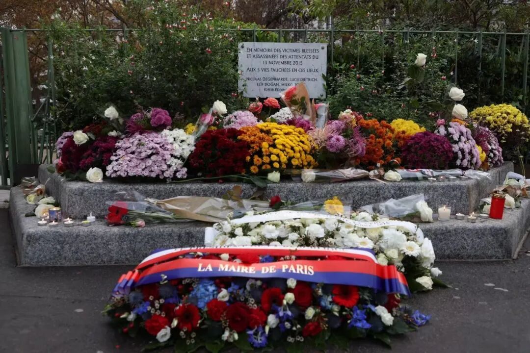 ▲ 2025年11月13日是2015年巴黎恐袭十周年纪念日,巴黎市政府举办众多活动进行纪念,大量巴黎民众也自发在众多与恐袭事件相关的地点进行悼念。图为法国总统马克龙与巴黎市长伊达尔戈在当年发生枪击的毕查街以南国王喷泉街 Café Bonne Bière餐厅附近的纪念点敬献的花篮。(欧洲时报 记者马行健摄)