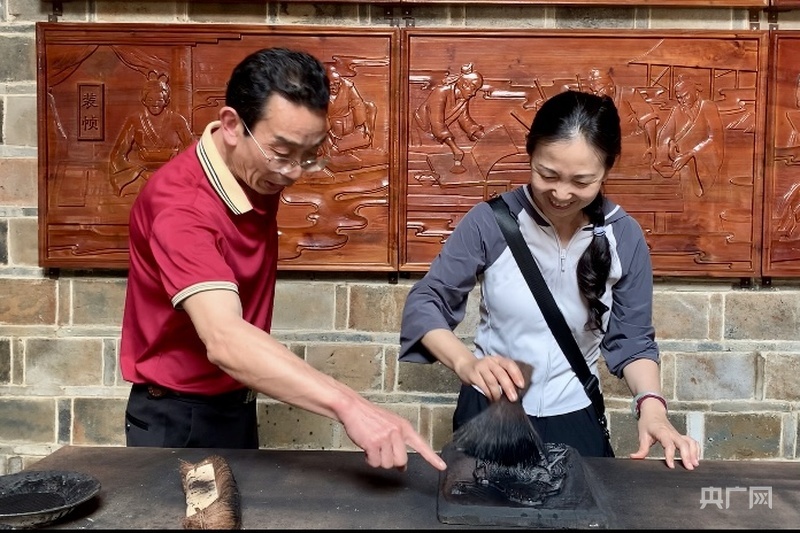 黄行忠（左）指导游客体验雕版印刷（央广网记者 罗晓英 摄）