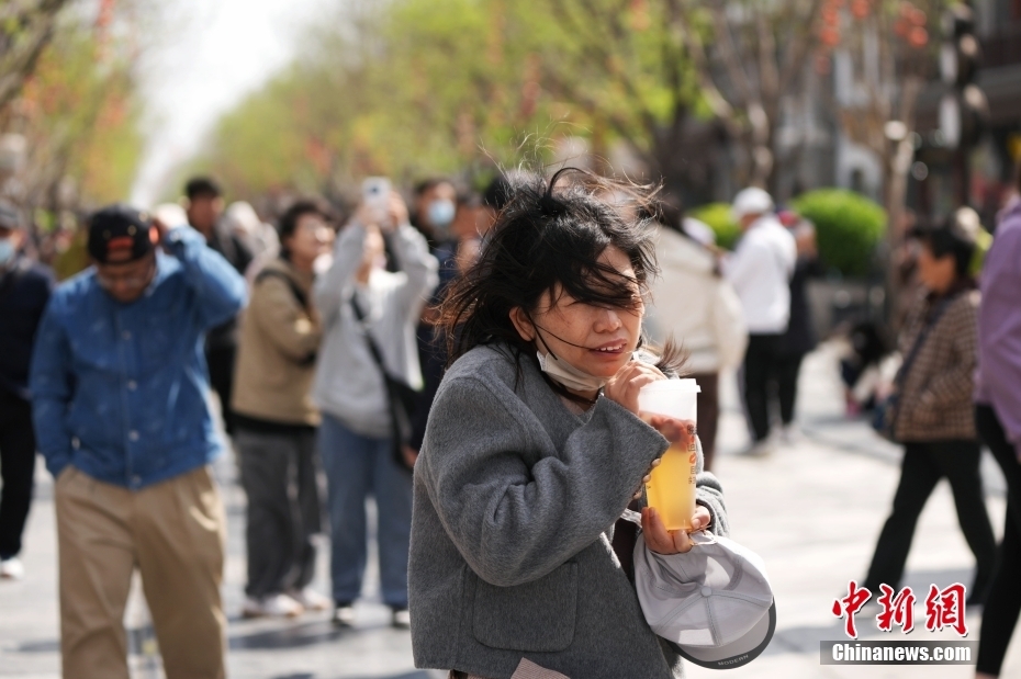 4月12日，民众在北京前门大街顶风出行。当日，北京大风橙色预警信号持续生效，6时至22时为风力最强时段。中新社记者 张祥毅 摄