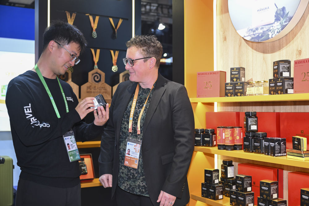 11月6日,在第八届进博会农食产品展区一家新西兰蜂蜜品牌展台,参展商(右)向观众介绍蜂蜜产品。新华社记者 陈浩明 摄