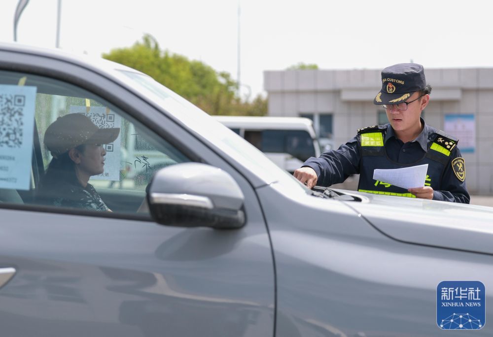 在新疆霍尔果斯公路口岸海关集中查验场,霍尔果斯海关工作人员(右)查验一辆由“摆渡人”驾驶出境的车辆的相关信息(5月28日摄)。2024年10月,霍尔果斯公路口岸正式施行“自驾出口商品车快速通关模式”,企业可以在线上生成包含车辆各类信息的二维码,通关时享受“一扫即过”的便捷服务。