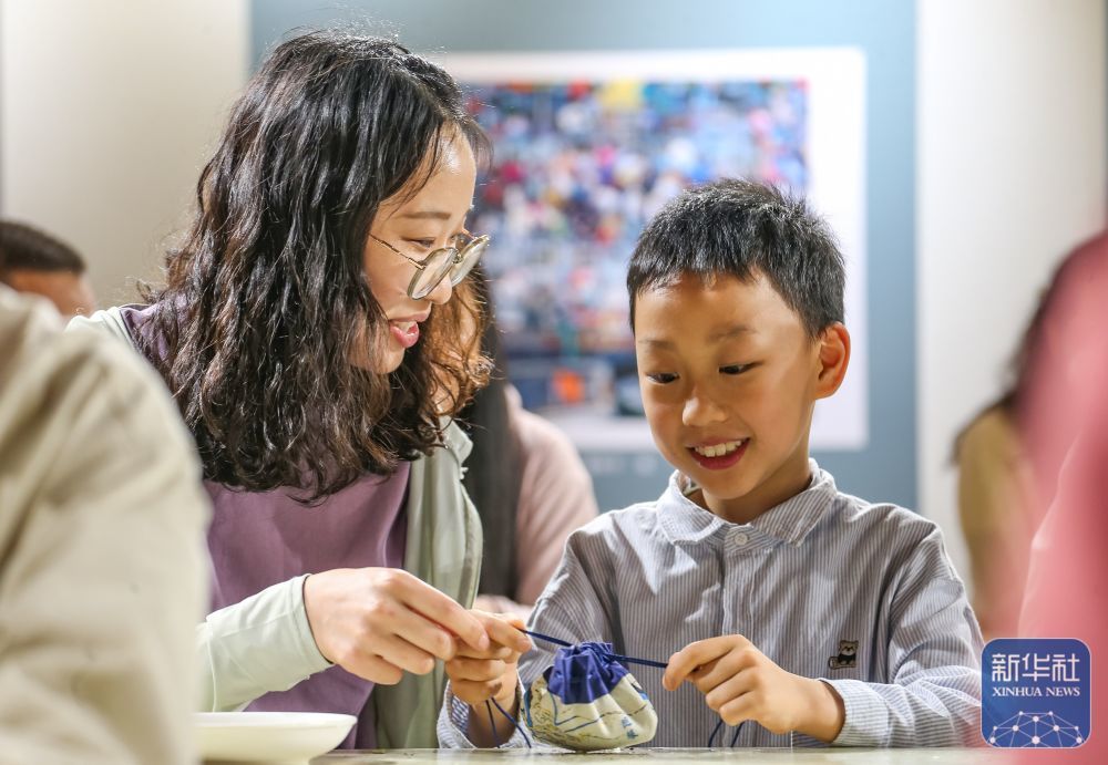 ↑ 5月23日，在江苏省句容市葛仙湖公园，小朋友与家长体验香囊制作。新华社发（钟学满摄）