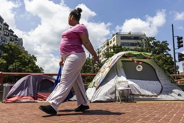 一名行人走过华盛顿环岛无家可归者的帐篷。美国总统特朗普在白宫新闻发布会上宣布,将在华盛顿特区部署国民警卫队,声称该地区的犯罪“失控”,誓言要清除首都的无家可归者营地。