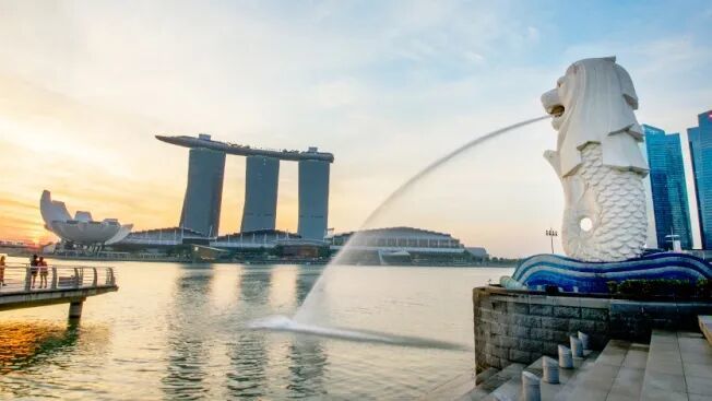 白天,鱼尾狮往新加坡河 (Singapore River) 喷出水流,背景是新加坡天际线