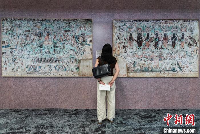图为一位女士参观莫高窟第220窟《西方净土变》(左)和《东方净土变》（右）的石窟壁画复制品　中新网记者　侯宇　摄
