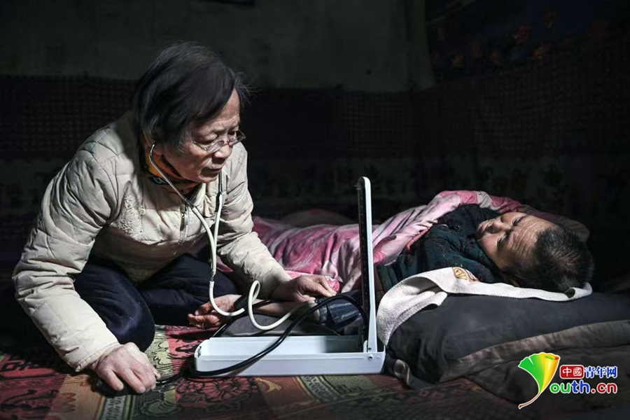 路生梅跪坐在土坑上为瘫痪不起的村民义诊。受访者供图