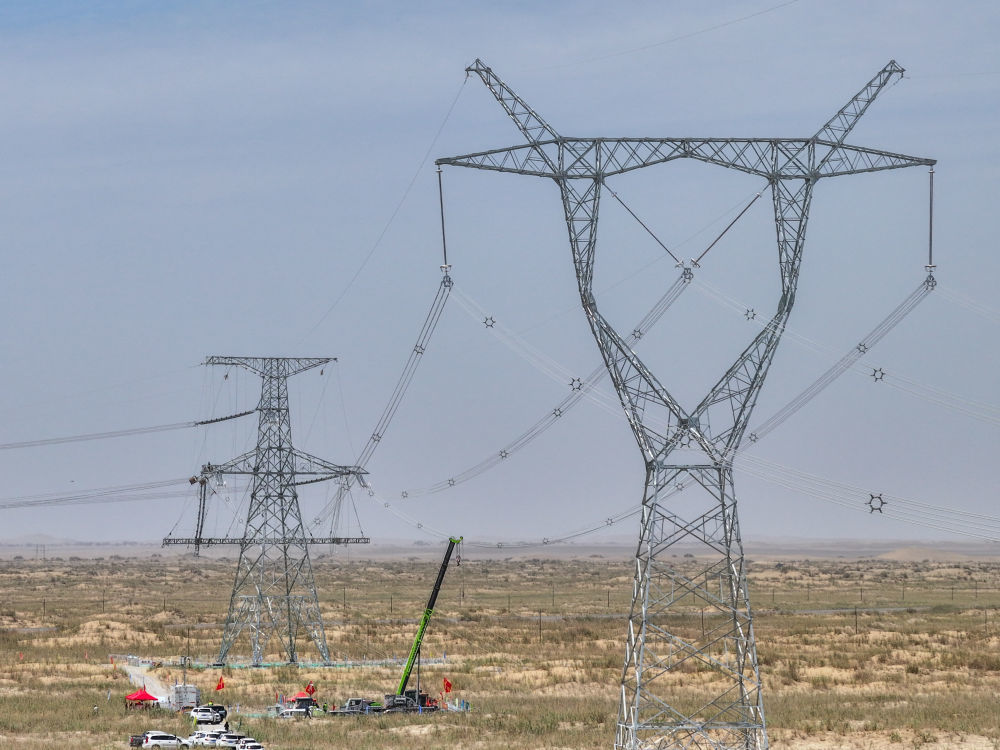 2025年7月13日,在塔里木盆地南缘的新疆和田地区民丰县,随着牵引机将最后一段电线成功从183号铁塔拽至188号铁塔,历时15年建设的环塔里木盆地750千伏输变电工程全线贯通(无人机照片)。新华社记者 丁磊 摄