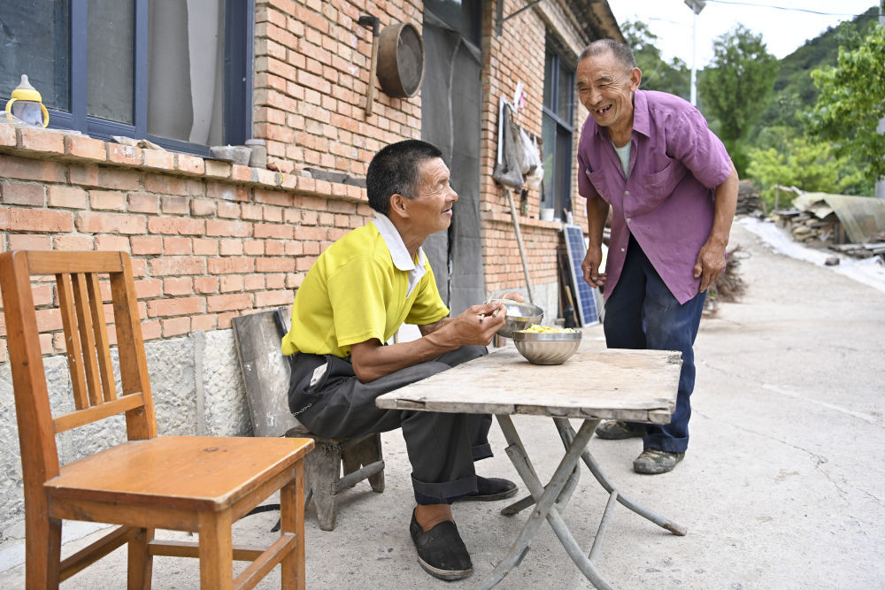 ↑村民元有才（右）为秦海松准备好午餐后，两人开心交流（2025年8月6日摄）。