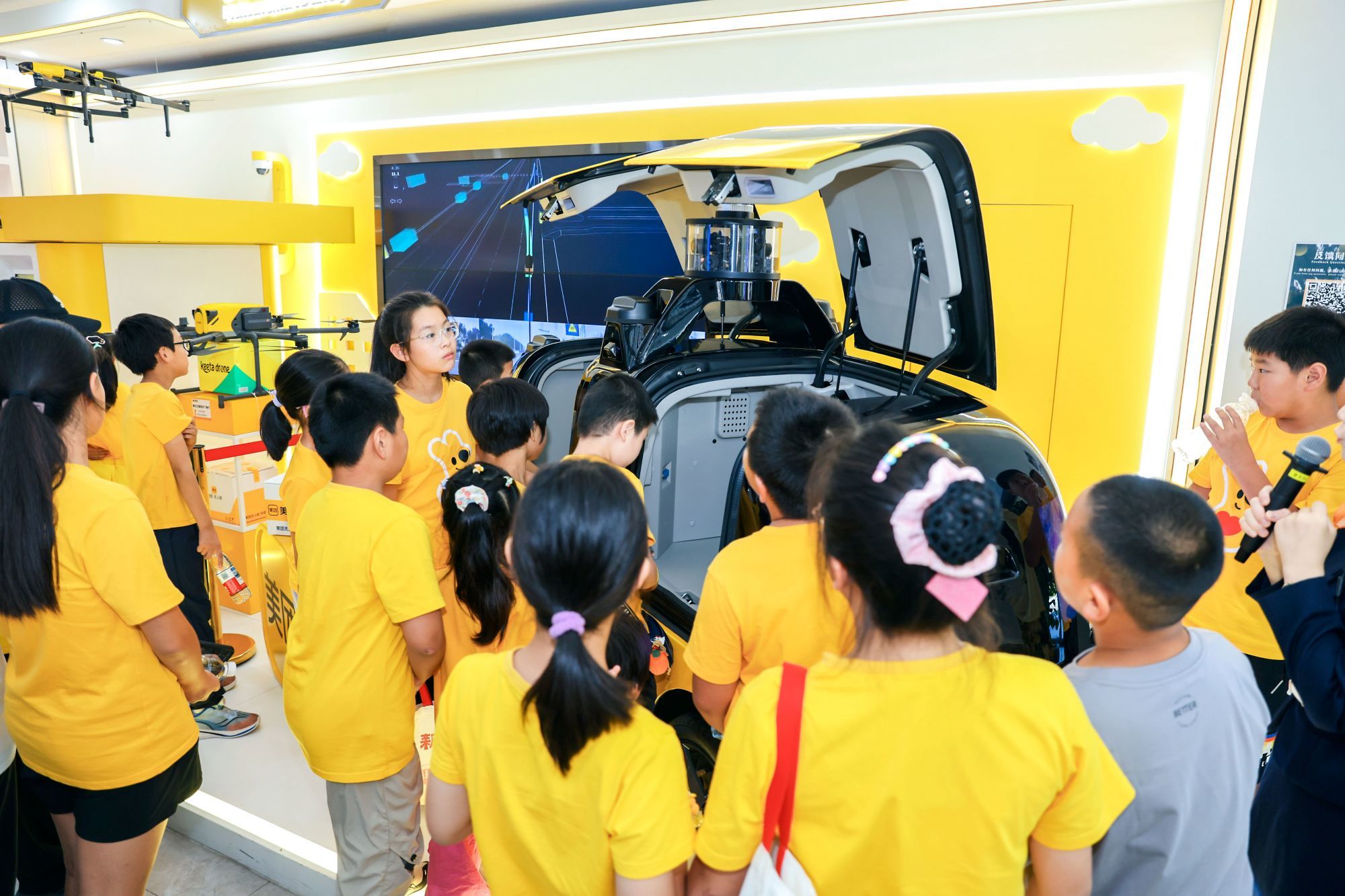 在美团总部的科技主题展区，孩子们正在了解无人车和无人机如何传送“空中快递”。