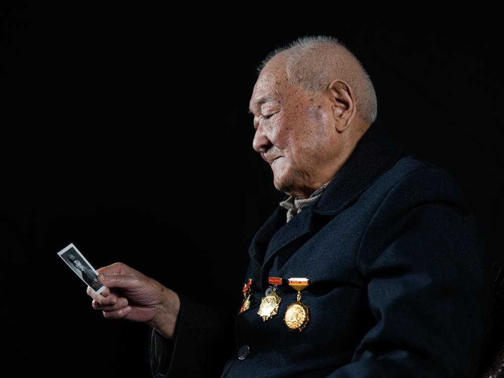 ↑刘寿山端详自己年轻时的军装照（4月9日摄）。