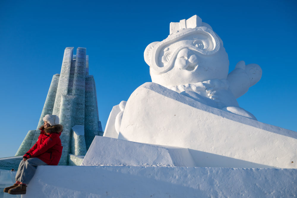 ↑1月3日，在哈尔滨冰雪大世界园区，游客与亚冬会吉祥物雪雕“妮妮”合影。新华社记者 张涛 摄